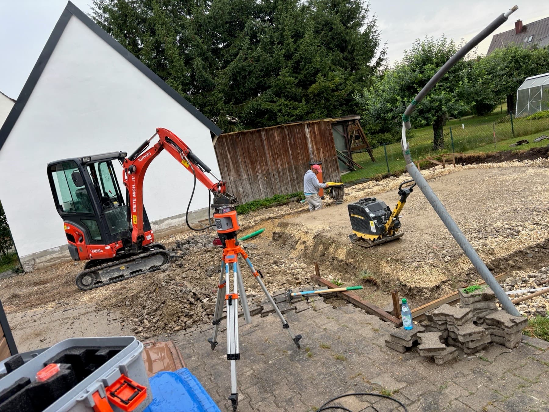 Baustelle mit Bagger, Rüttelplatte und Nivelliergerät